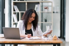 Mulher sorridente organizando finanças em um escritório, usando uma calculadora e escrevendo em papéis.